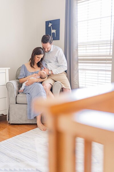 mom & dad sitting by the couch looking at baby taken by a  lifestyle newborn photographer in Northern Virginia