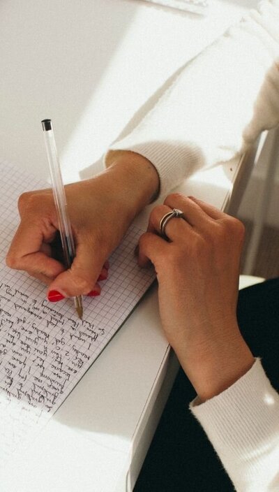 Close-up of Kaya’s hands writing in a grid notebook with a black pen.