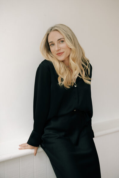 Black and white photo  of Fallon Stovall sitting in a chair holding a blazer over her shoulders