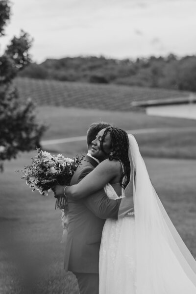 A newlywed couple hugging while one holds a bouquet of flowers 