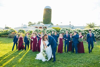 Bride and groom kiss with celebrating bridal party in background sinkland farms venue