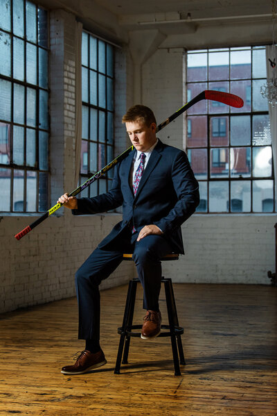 senior photo of athlete wearing suit and holding hockey stick