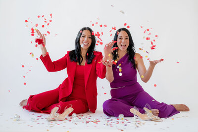 Stef and Tara sitting on floor throwing confetti in air
