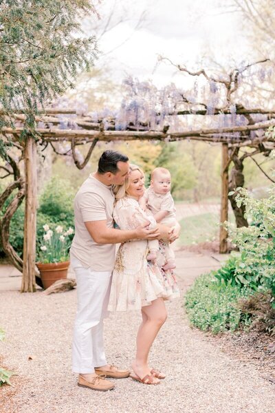 A famiy of three stands under an arbor covered in wisteria during their NJ family photos.