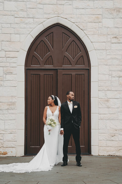 bride and groom standing in front of large doors