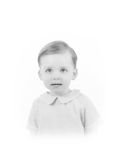Black and white heirloom portrait of a smiling baby dressed in a classic white outfit with lace details. This timeless baby photography captures the innocence and joy of childhood, created by a Birmingham newborn photographer specializing in elegant, light-filled portraits.