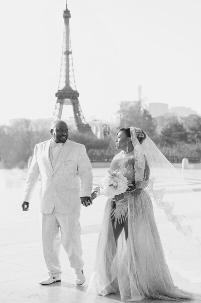 A bride and groom walk by the Eiffel Tower in Paris on their wedding day