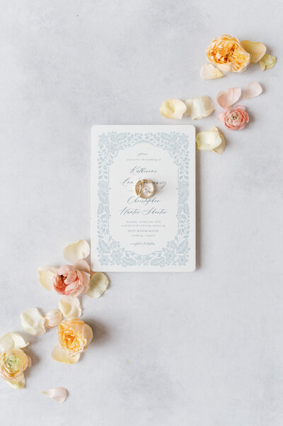 flat lay of wedding rings resting on top of an invitation with flower petals surrounding the scene