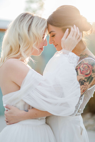 Two brides hold each other as they have their foreheads touching and one bride has her hands in the others' hair