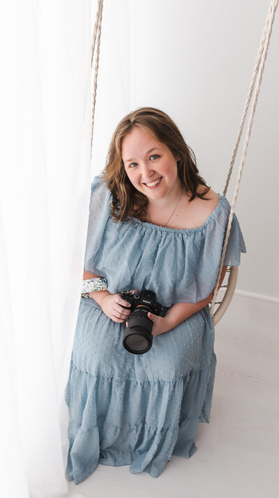 Woman in flowy dress holding camera smiling, taken by Stickan Photography as an Andover Newborn Photographer