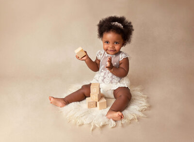 Baby girl is swaddles in a white wrap embellished with tulle and pearl detail, Her hands are peeking out of the wrap and folded under her chin.