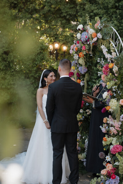 Candid photo of bride and groom looking at each other during wedding ceremony vows at Franciscan Gardens in San Juan Capistrano