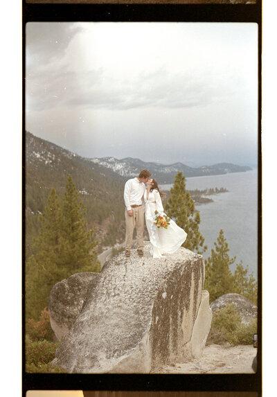 film photo of a man and woman in wedding attire kissing overlooking lake tahoe
