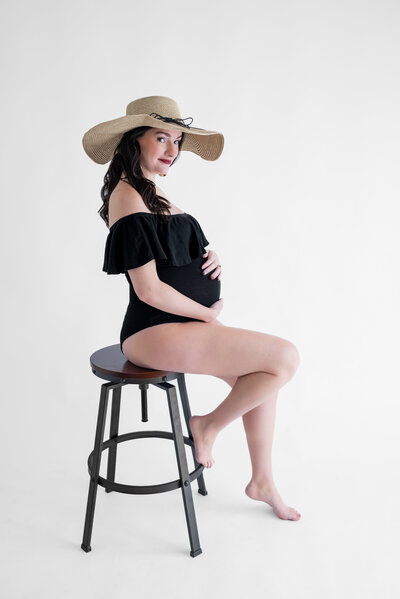 Pregnant woman poses on a stool for her maternity portraits in the Hampton Cove Studio