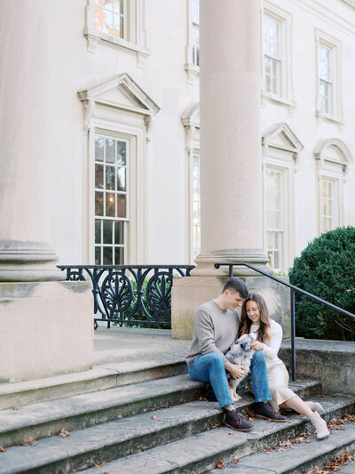 A man and woman sitting on the steps of a building and looking at their dog by Katie Stansfield Photography, a Richmond photographer.