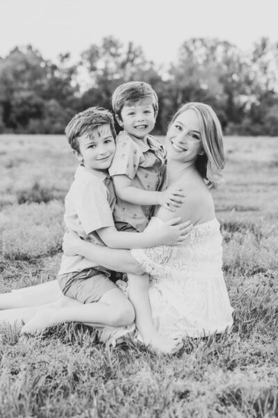 Valerie of Worth Capturing Photography poses with two young boys during motherhood outdoor portrait session