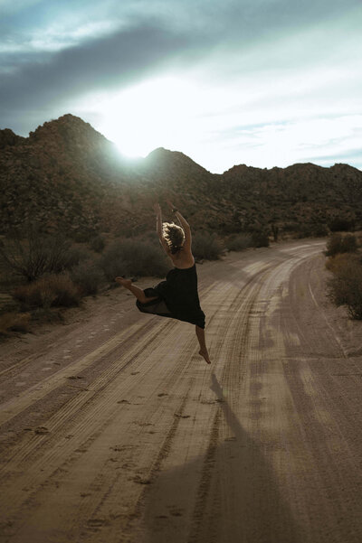 a woman dancing over a path with the sun glinting over hills on both sides