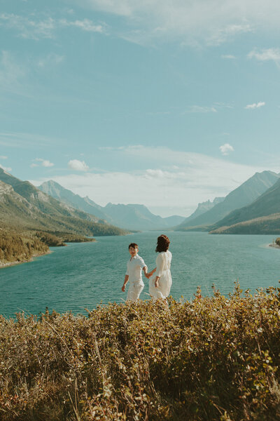 couple holds hands, walking across the  prince of wales hotel grounds, overlooking waterton lakes