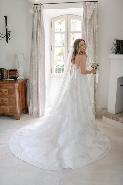 Black and white portrait of a bride on her wedding day, wearing a spaghetti strap, low scoop back fil-de-coupe gown from Lela Rose with a  Lily of the Valley bouquet