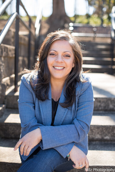 a woman dressed in a blue blazer posed on a set of stairs smiling at the camera photographed by Millz Photography in Greenville, SC