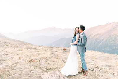 a bride and groom sharing a romantic snuggle on the top of  rocky mountain national park for a classic Colorado wedding photo on an epic mountain during sunrise