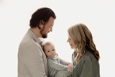 mom, dad and six month old baby sitting on a grey rug together leaning in closely together