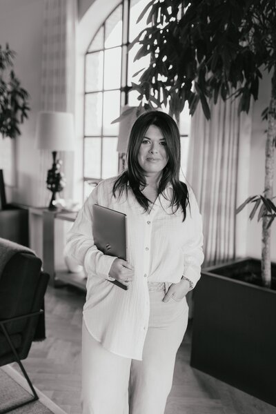 Sarah Hurja holding laptop  and smiling standing in living room.