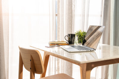 Image of a dining table with a laptop, mug, and books at it.