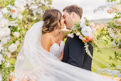 Bride and groom sharing a romantic kiss at their wedding in Littleton, Colorado at the Arrowhead Golf Course with her veil flowing.
