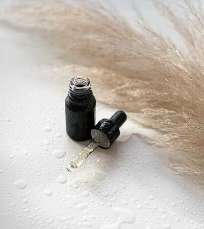 Flacon en verre noir, pipette remplie d'huile essentielle posée à côté, gouttes d'eau autour.