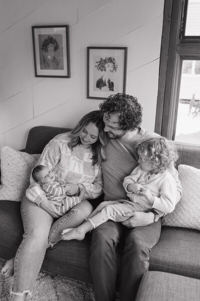 man and woman sitting on a couch holding their two children