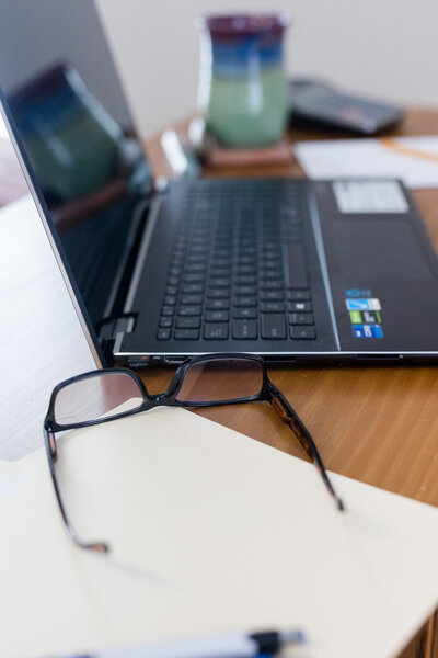 Lap top sitting on a desk next to a pair of glasses