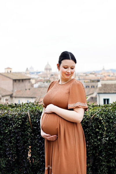 A pregnant woman looking down to the side while holding her belly. Taken by Rome Photographer, Tricia Anne Photography.