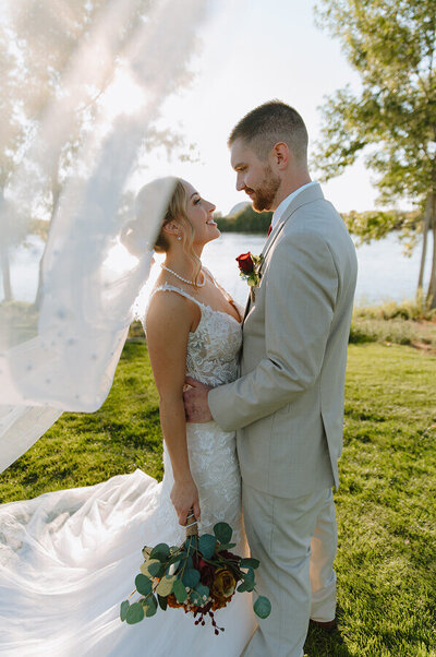 Bridal portraits of a bride and groom on their wedding day. The groom is holding the waist of his bride as her veil sweeps up into the sky.