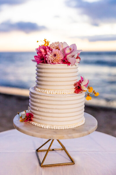 Elegant, simple wedding cake set against the breathtaking ocean backdrop at Mauna Lani Auberge, capturing the essence of a luxury bespoke celebration in Hawaii