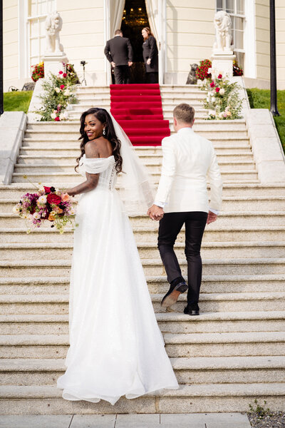 Bride and groom walking up a staircase with red carpet at The K Club in Kildare, Ireland