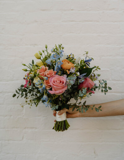 Bouquet of flowers is held in front of white brick wall in Georgetown washington d.c.