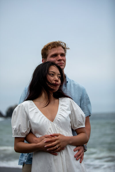 Engaged couple shares an embrace on the beach in California for their engagement photo session.