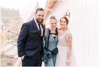 photographer standing between bride and groom outside of the venue laughing together