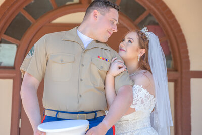 Bride in white dress and groom in marine corps uniform pose for a photo by Scranton Wedding Photographer Eric Boylan in front of a red stucco building at Nay Aug Park in Scranton, Pa