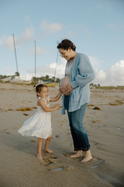pregnant mom plays on beach with her daughter