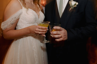A bride and groom pose for a photo with their drinks at cocktail hour.