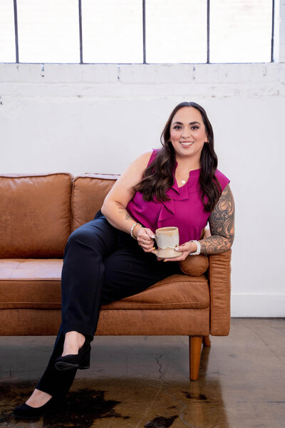 Stephanie, Founder of BCWise Consulting, sitting on a leather sofa drinking coffee