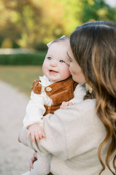 mom kisses baby girl on the cheek and baby smiles during photography session with Worth Capturing