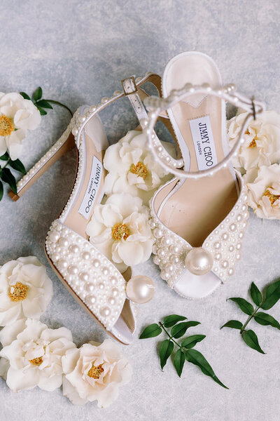 Jimmy Choo pearl wedding shoes surrounded by white flowers.