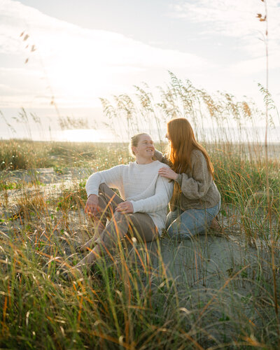 Man and Woman are sitting together in the sand on the beach in Charleston, South Carolina for their engagement photographs created by Sarah Woods Photography.