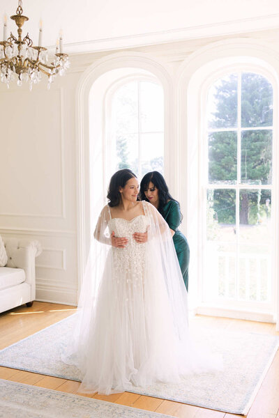 Bride and mother getting ready for a wedding. Mother is helping the bride with her dress.
