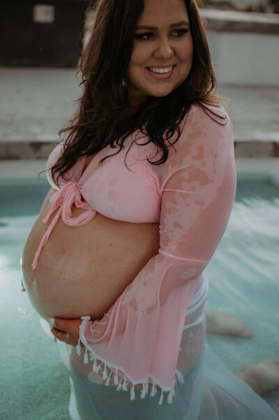San Diego Maternity, Pregnant woman smiling, holding her baby bump. Backyard San Diego Pool set.