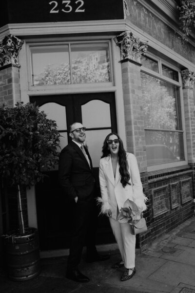 A bride and groom at their short legal ceremony in London. The bride is wearing a custom white suit for her city wedding the day before her big celebrant lead wedding. 