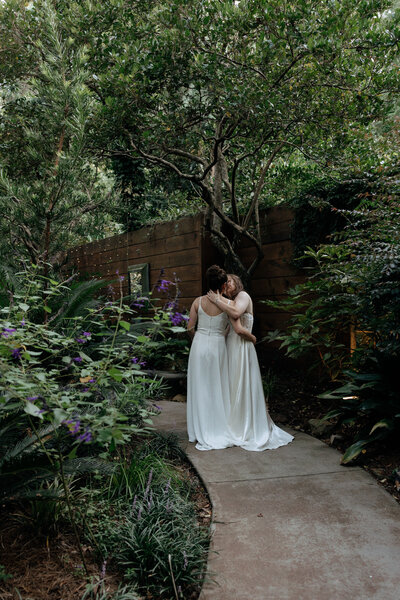 Two brides share a kiss after their ceremony surrounded by the beautiful garden at the River Road and Jasmine House in South Carolina.